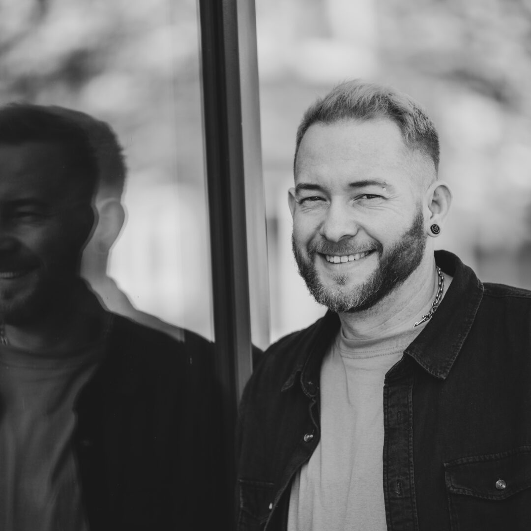 Sascha Mylenbusch Exklusiv Hair & Style - Ihr exklusiver Damenfriseur in Düsseldorf, Benrath - Portraitfoto von Sascha Mylenbusch in Düsseldorf vor einem Fenster schwarz-weiss