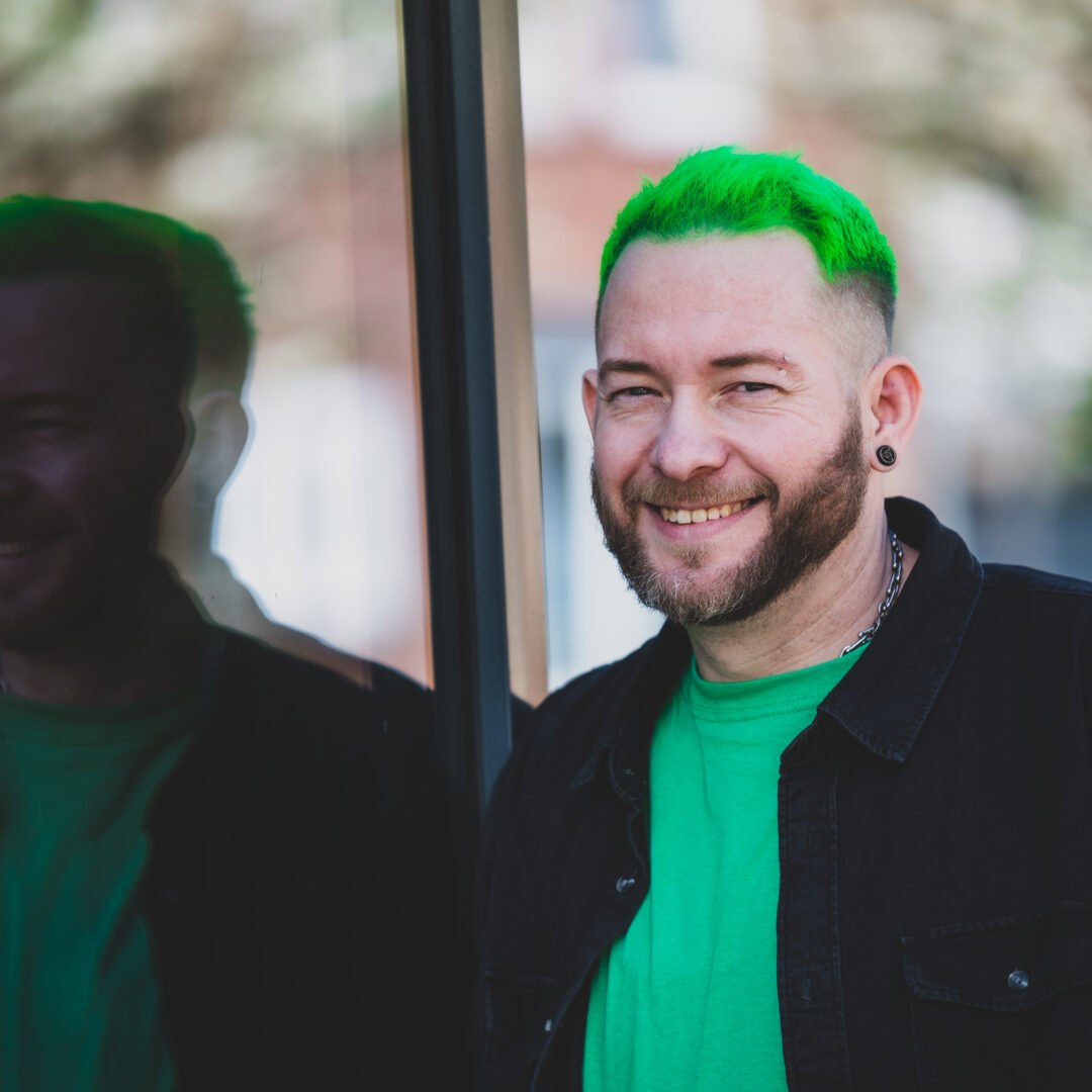 Sascha Mylenbusch Exklusiv Hair & Style - Ihr exklusiver Damenfriseur in Düsseldorf, Benrath - Portraitfoto von Sascha Mylenbusch in Düsseldorf vor einem Fenster.