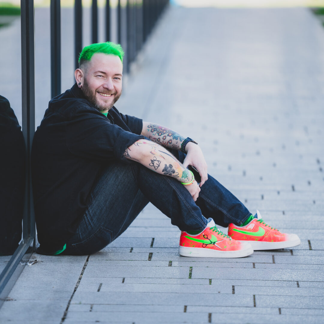 Sascha Mylenbusch Exklusiv Hair & Style - Ihr exklusiver Damenfriseur in Düsseldorf, Benrath - Portraitfoto von Sascha Mylenbusch in Düsseldorf sitzt vor einem Fenster.