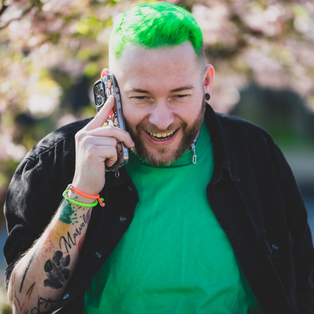 Portraitfoto von Sascha Mylenbusch in Düsseldorf unter einem Kirschblütenbaum mit dem Telefon